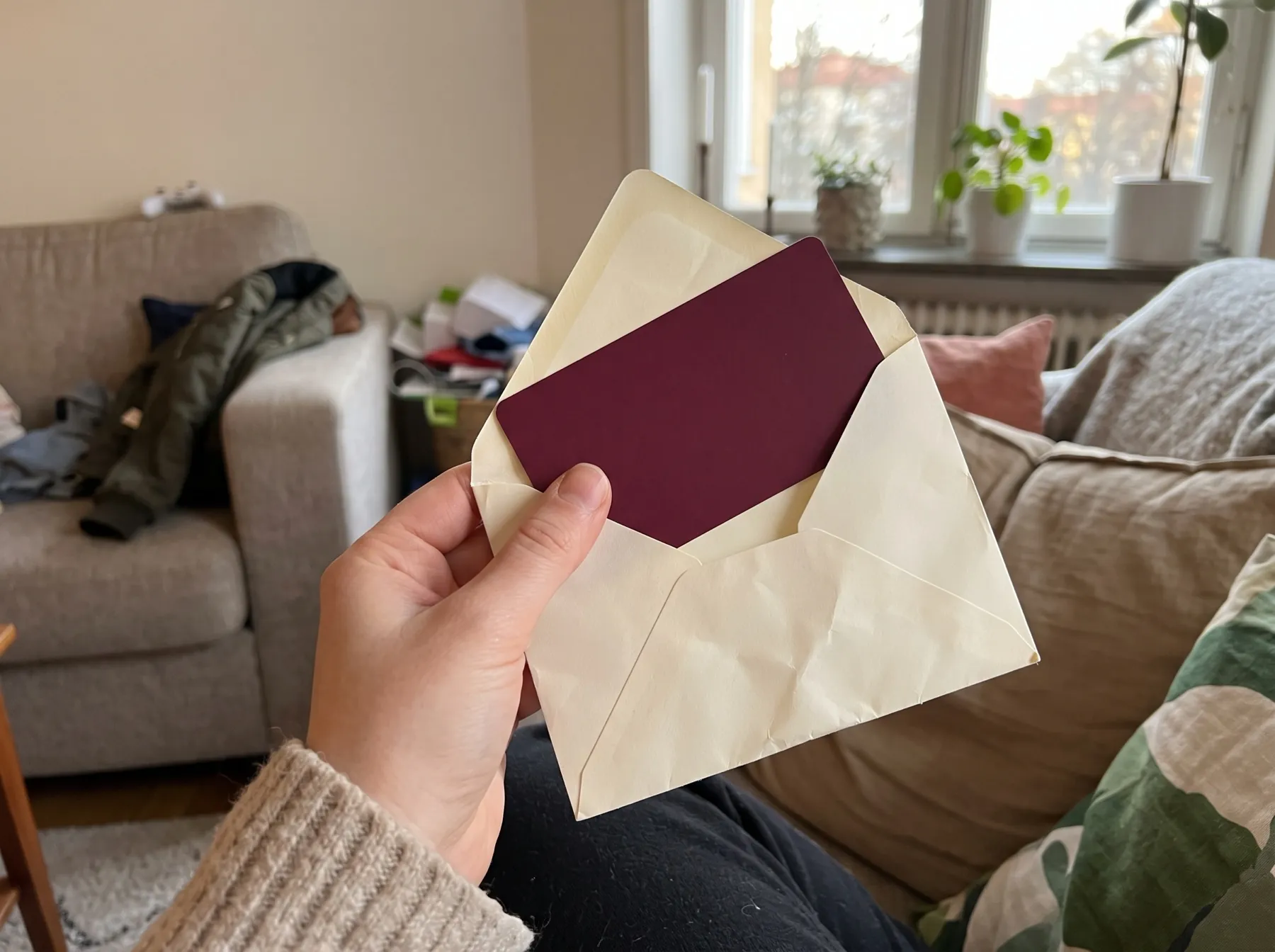 En hand håller ett öppnat kuvert med ett vinrött presentkort från Decanto
